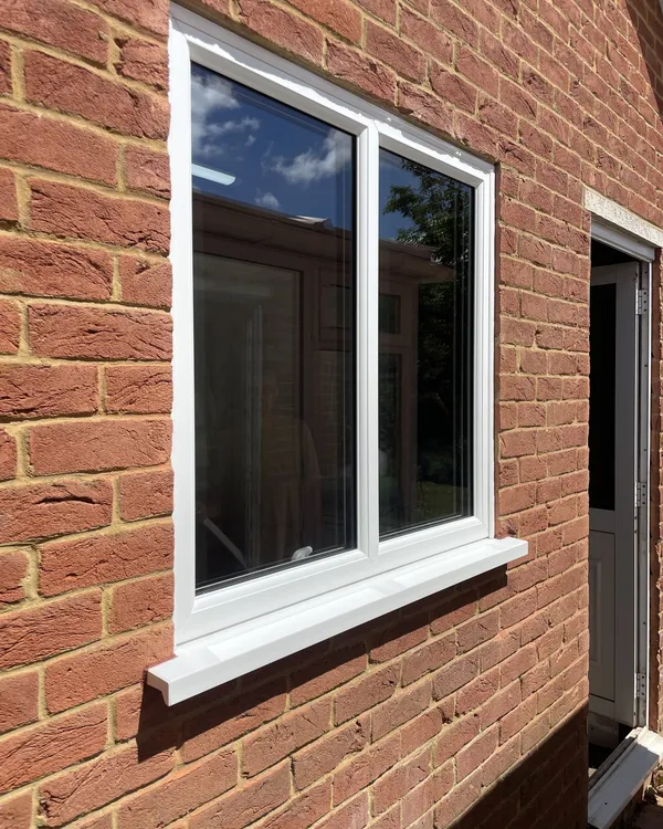 White uPVC casement window with a projecting sill fitted in a red brick wall.