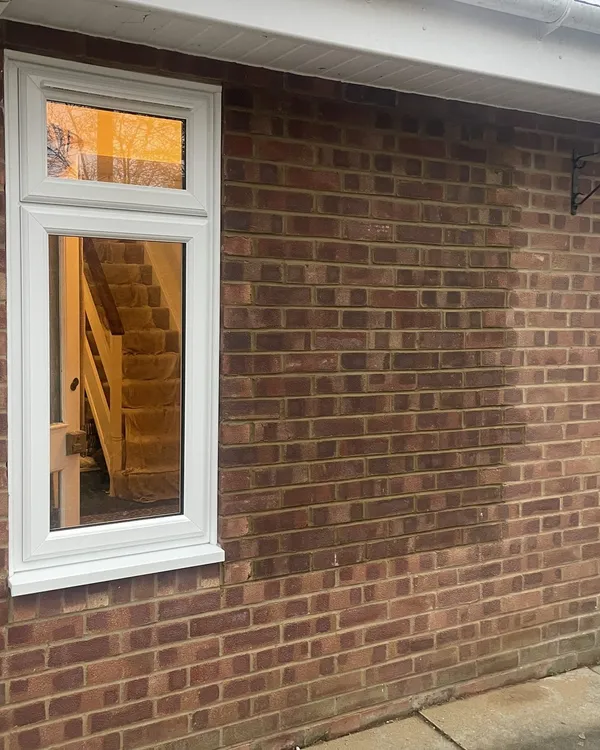 Tall white uPVC window with a toplight fitted in a red brick wall, with a staircase visible inside.
