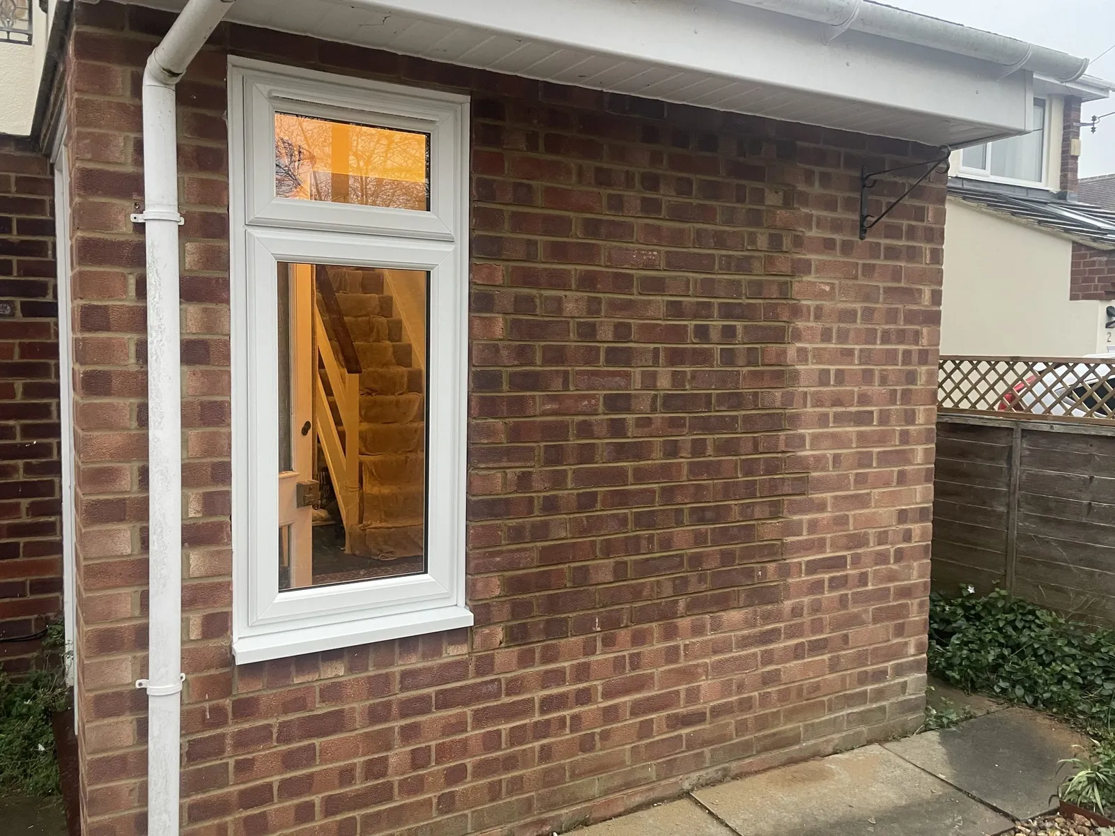 Tall white uPVC window with a toplight fitted in a red brick wall, with a staircase visible inside.