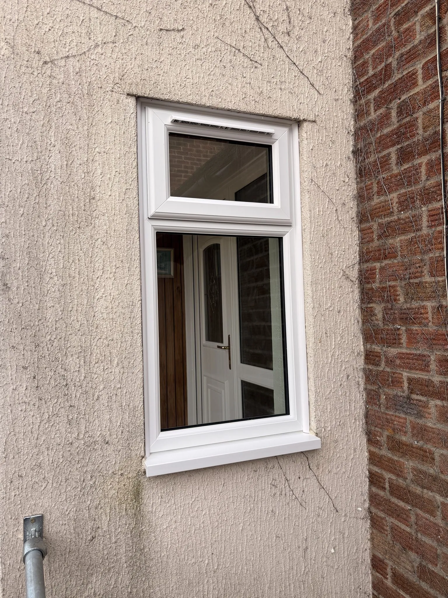 White uPVC window with an opening toplight fitted in a pebbledash rendered wall.