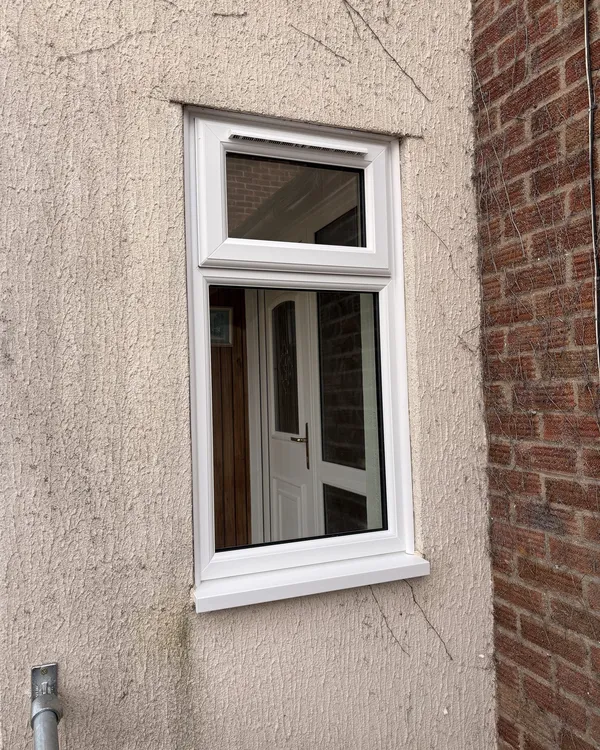 White uPVC window with an opening toplight fitted in a pebbledash rendered wall.
