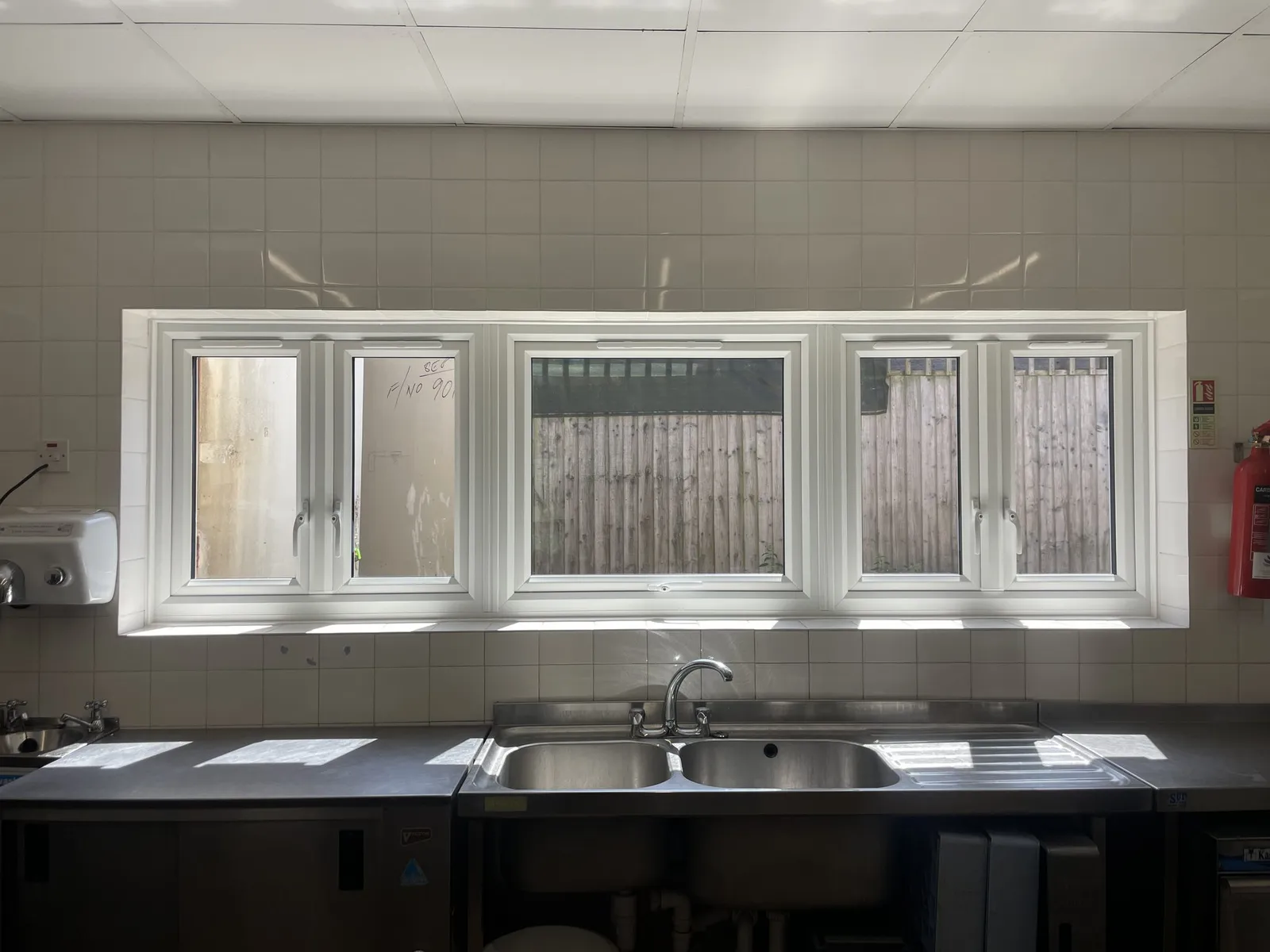 Run of white uPVC casement windows fitted above the sinks of a tiled commercial kitchen.