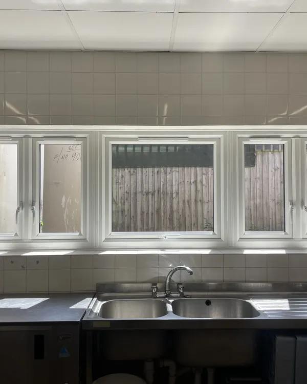 Run of white uPVC casement windows fitted above the sinks of a tiled commercial kitchen.