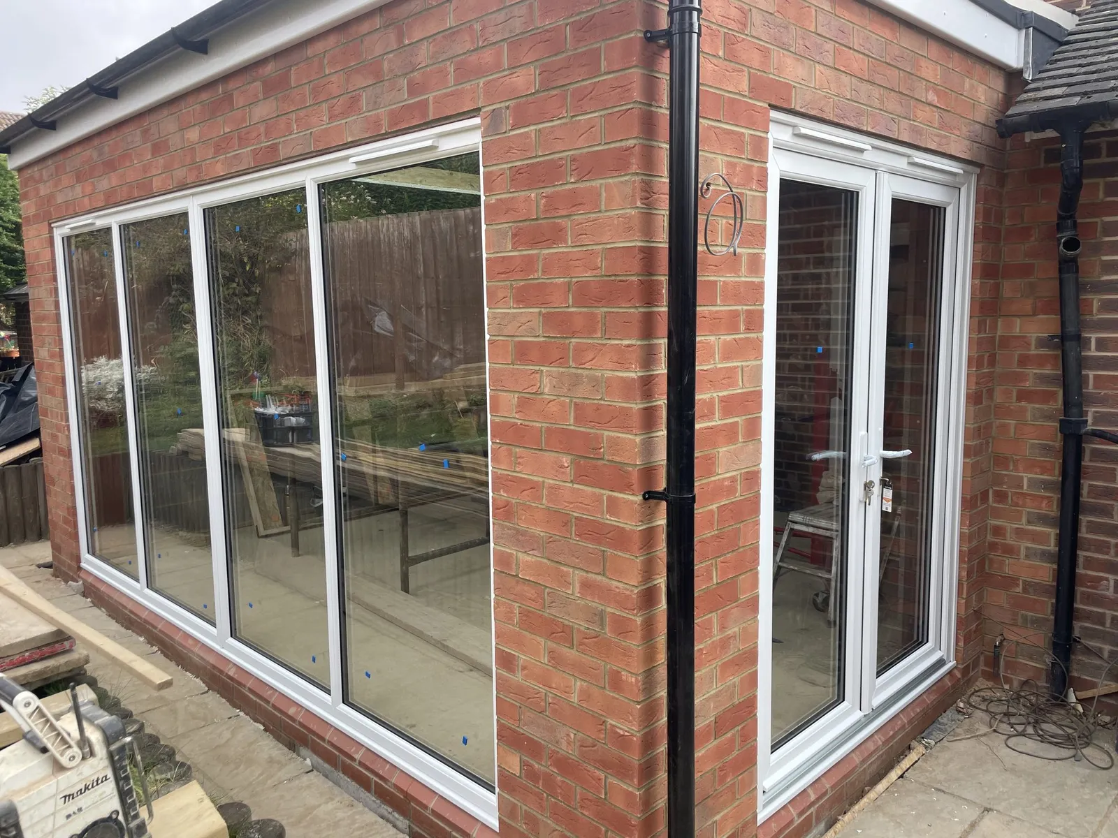 New red brick extension fitted with a run of tall white uPVC windows and a pair of white French doors at the side.