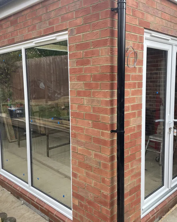 New red brick extension fitted with a run of tall white uPVC windows and a pair of white French doors at the side.