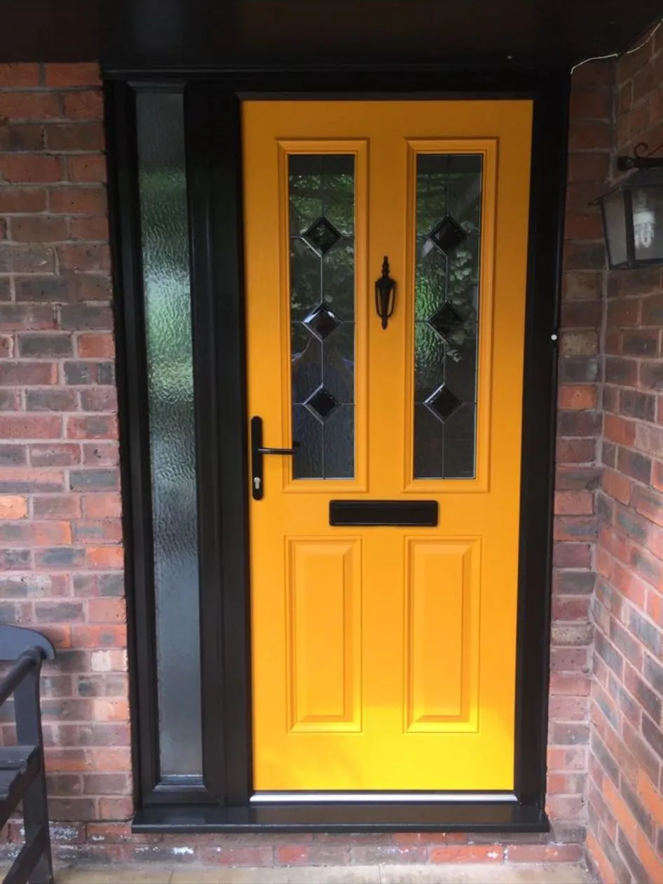 Bright yellow composite front door with diamond glass detail and black handle, fitted in a black frame with a glazed side panel.